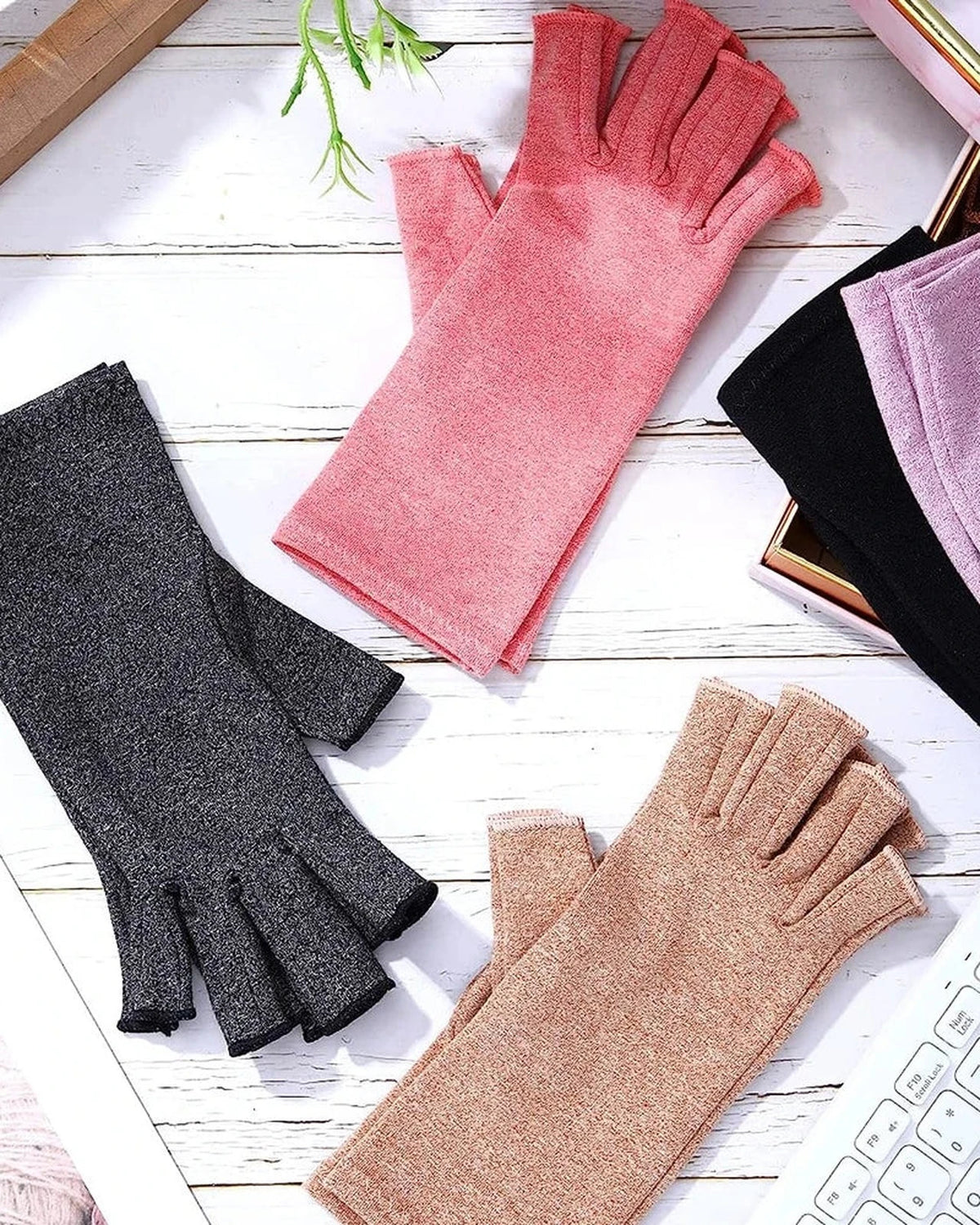 Fingerless compression gloves in gray, pink, beige, black and purple laid on a desk