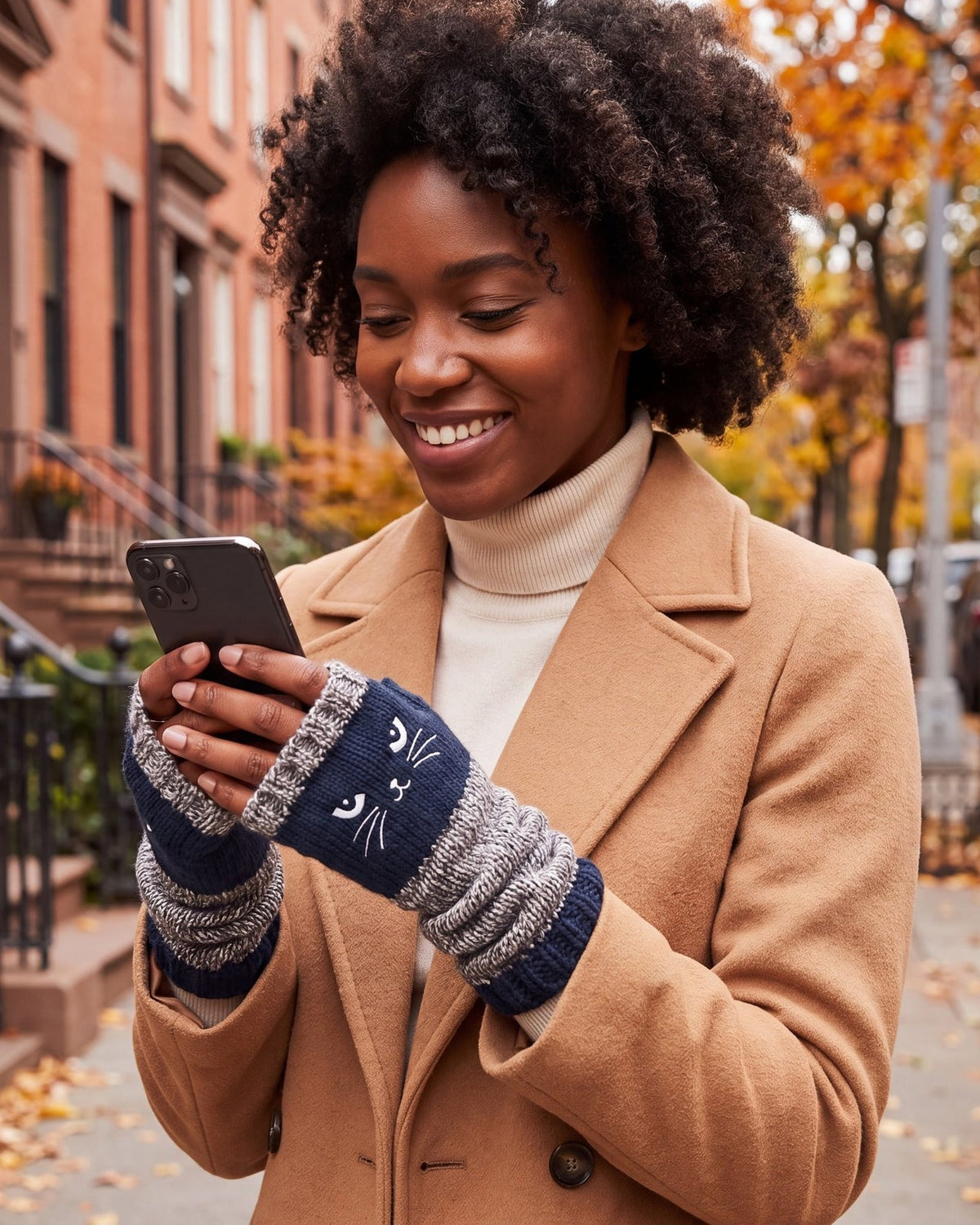 Woman texting on her phone in navy cat fingerless gloves on a city street