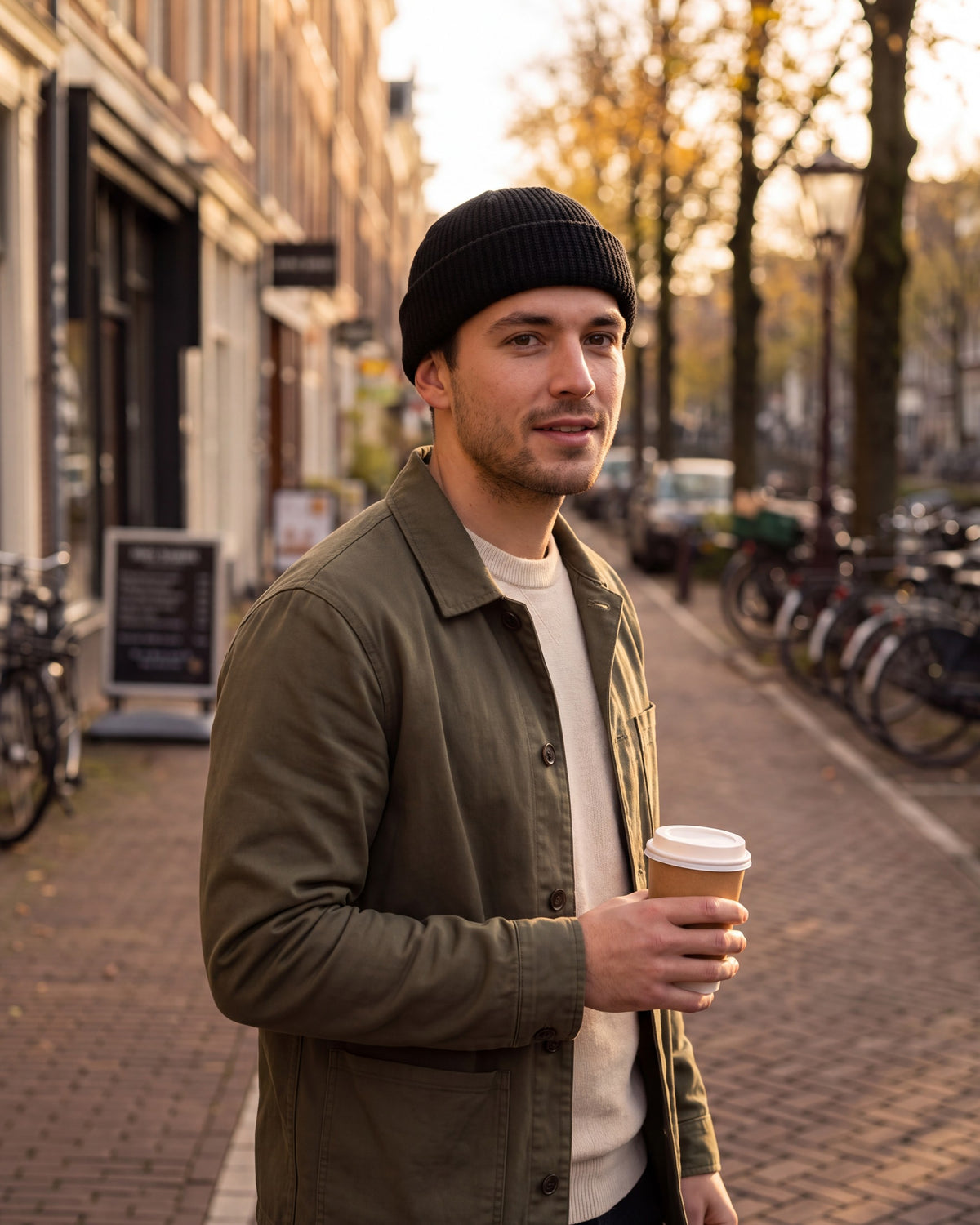 Man in a black fisherman beanie walking with a coffee on a city street