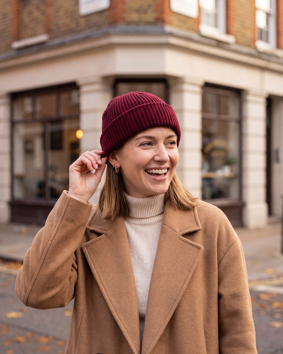 Woman laughing in a wine red fisherman beanie on a city street
