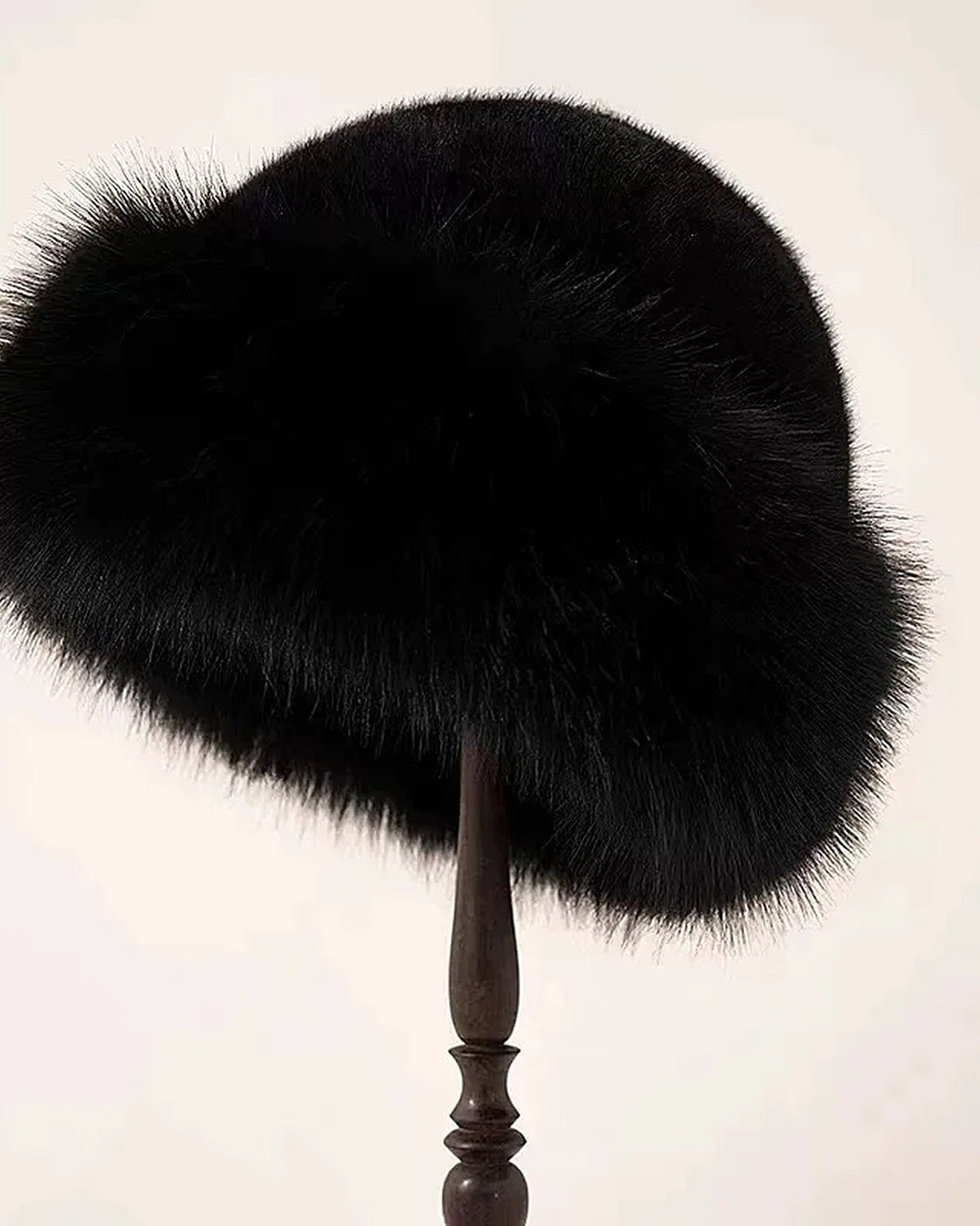 Black faux fur hat with rolled brim on a hat stand