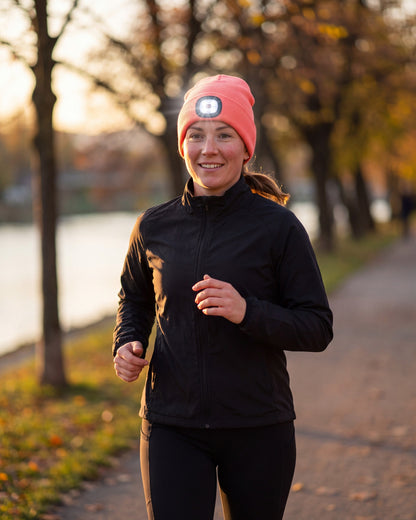 Woman running on a riverside path at golden hour in a pink LED beanie with the light switched on
