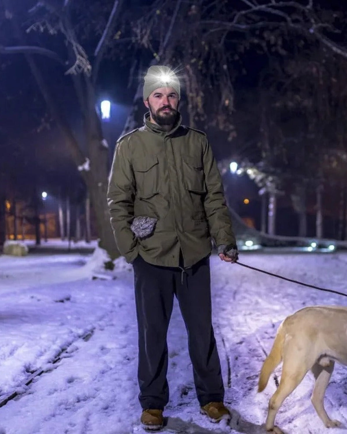 Man walking his dog in a park at night wearing an LED beanie with the light on