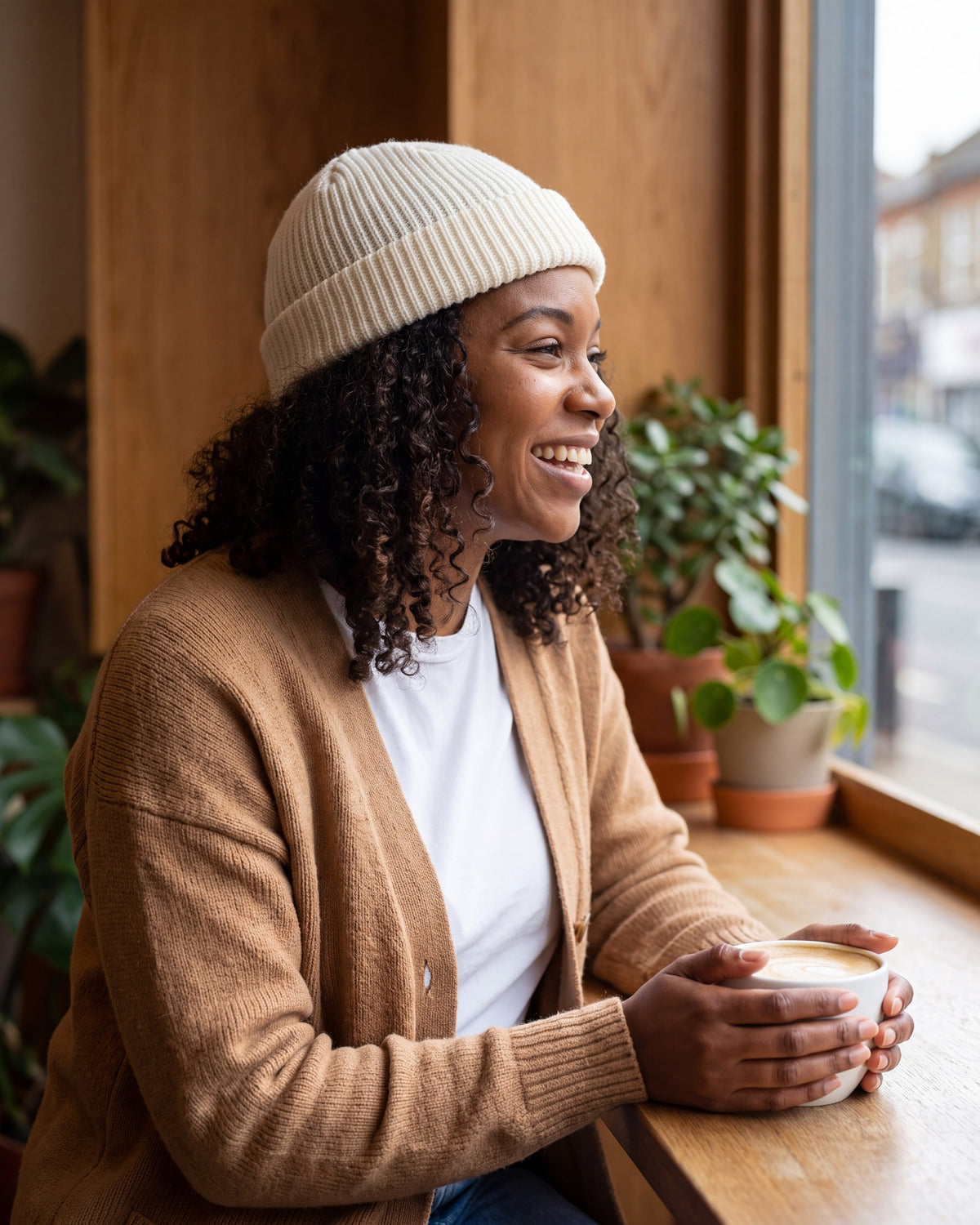 Woman laughing by a coffee shop window wearing a white short rib knit fisherman beanie