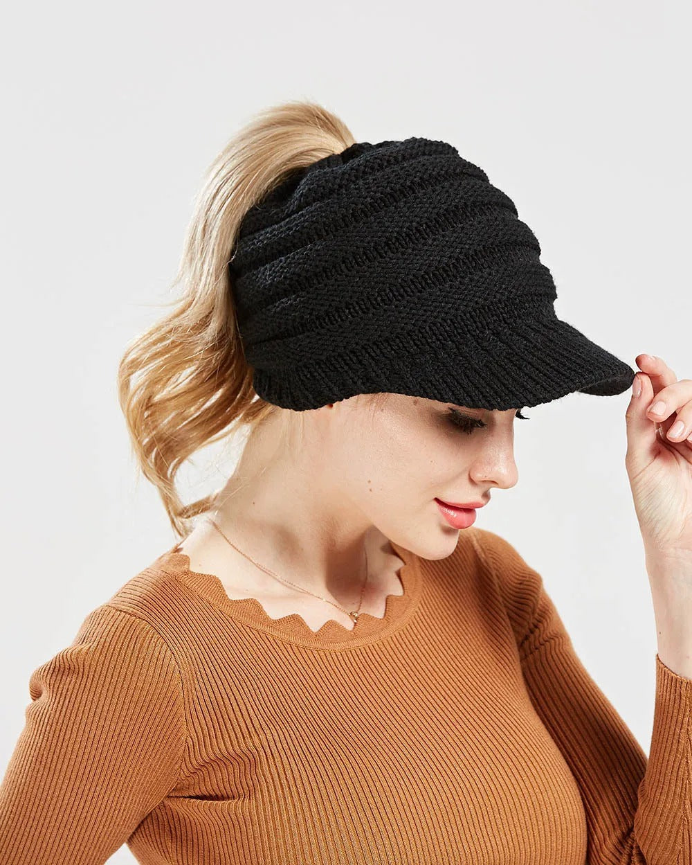 Woman wearing a black ponytail beanie with brim and her ponytail through the back