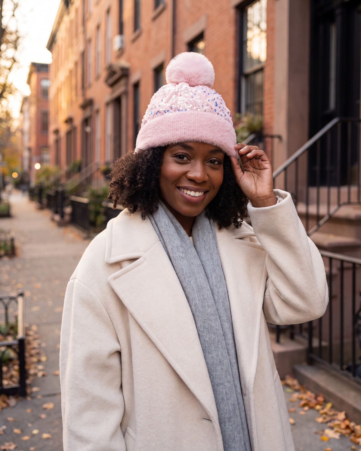 Woman adjusting a light pink sequin pom pom beanie on a city street