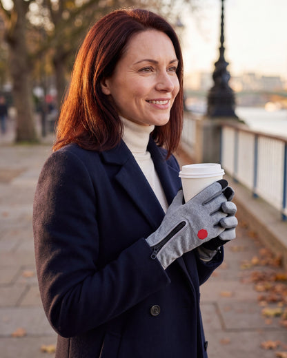 Woman holding a takeaway coffee on a riverside walk wearing gray thermal touchscreen gloves with zip cuffs