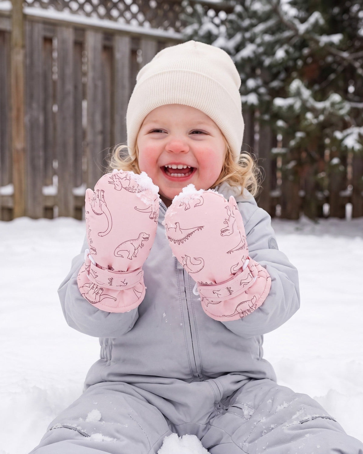 Laughing toddler girl playing outdoors in pink dinosaur print mittens