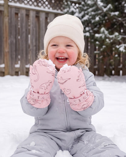 Laughing toddler girl playing outdoors in pink dinosaur print mittens